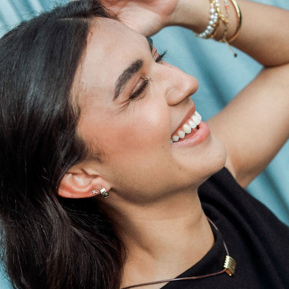 Woman with dark hair, earring stack and black top against a light blue background
