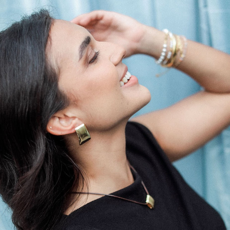 Woman wearing gold jewelry against a light blue curtain background