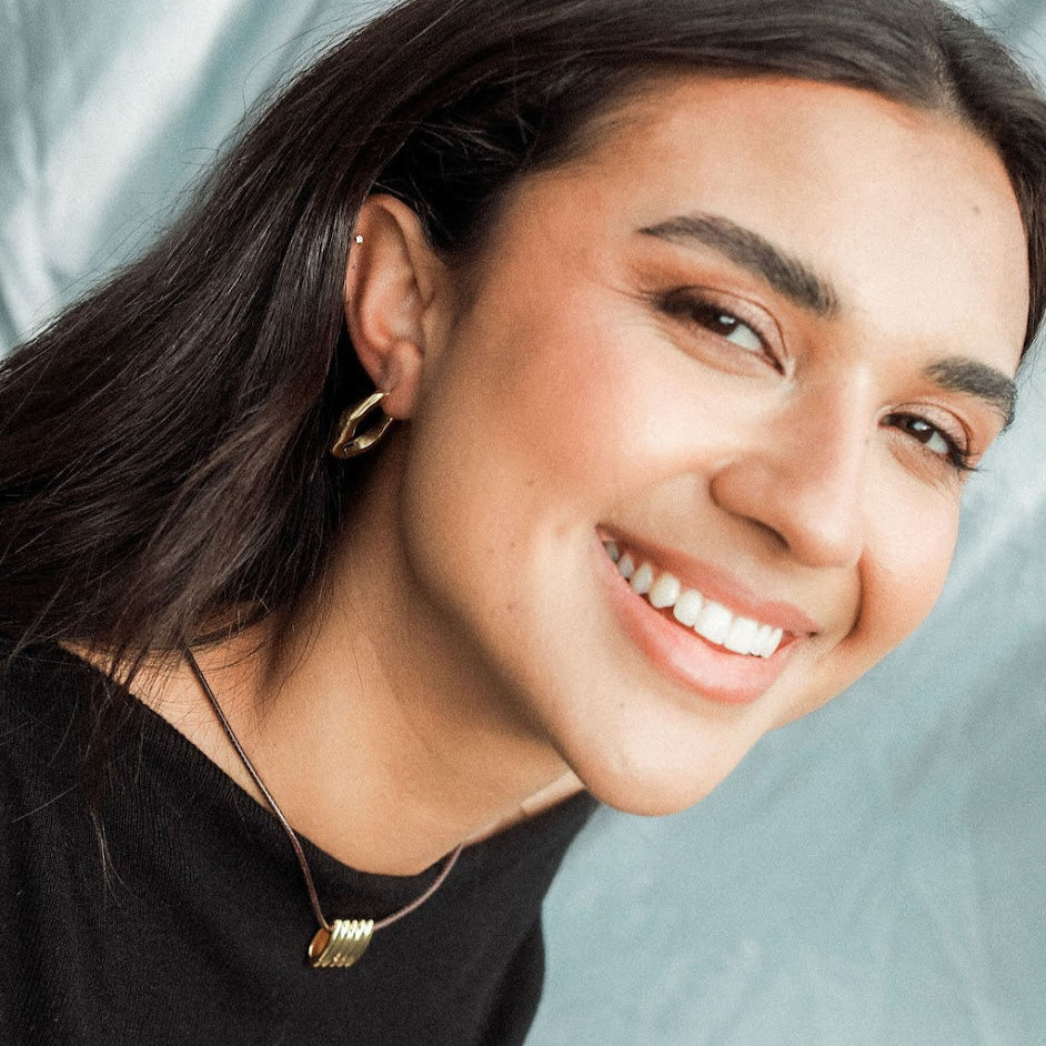 Woman with a smile and a cord pendant necklace against a light blue background