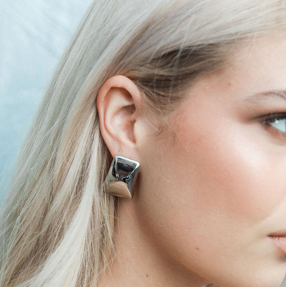 Close-up of a woman wearing a silver earring against a light blue background