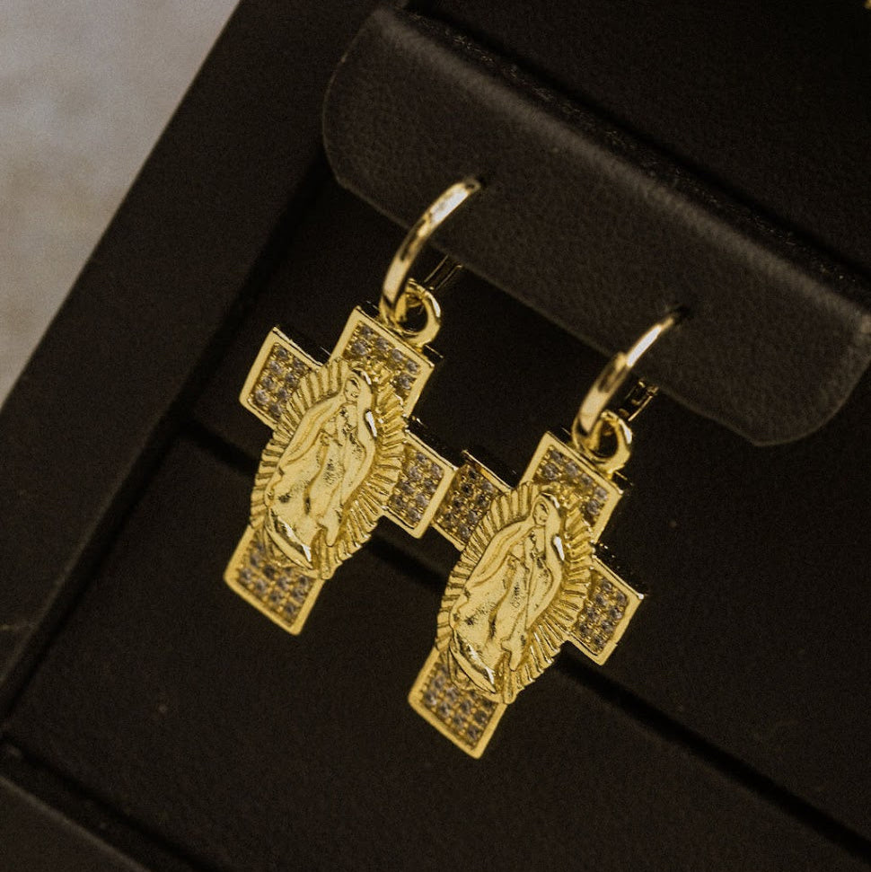 Gold cross-shaped earrings on a black jewelry box