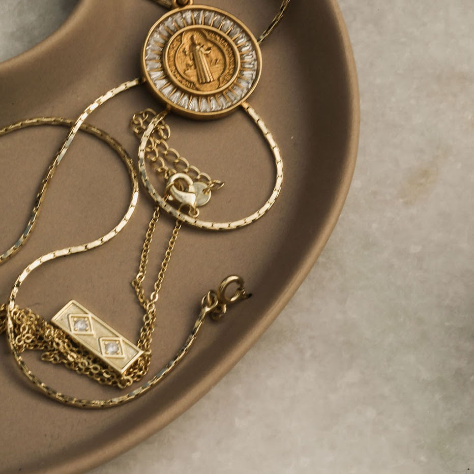 Gold necklaces with intricate designs on a brown ceramic dish.