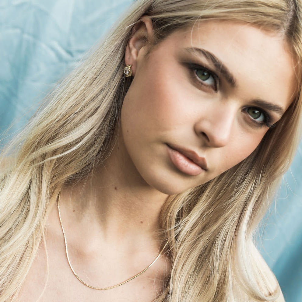 Woman with blonde hair fine chain and earrings against a light blue background