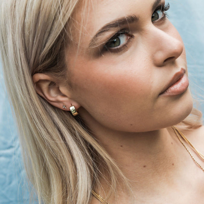 Woman with blonde hair and gold earrings and chain stack against a light blue background