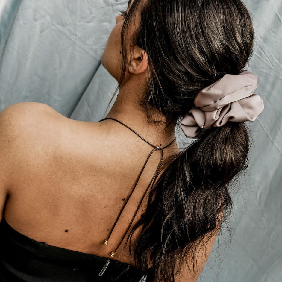 Woman with a ponytail wearing a scrunchie, black top against a gray background