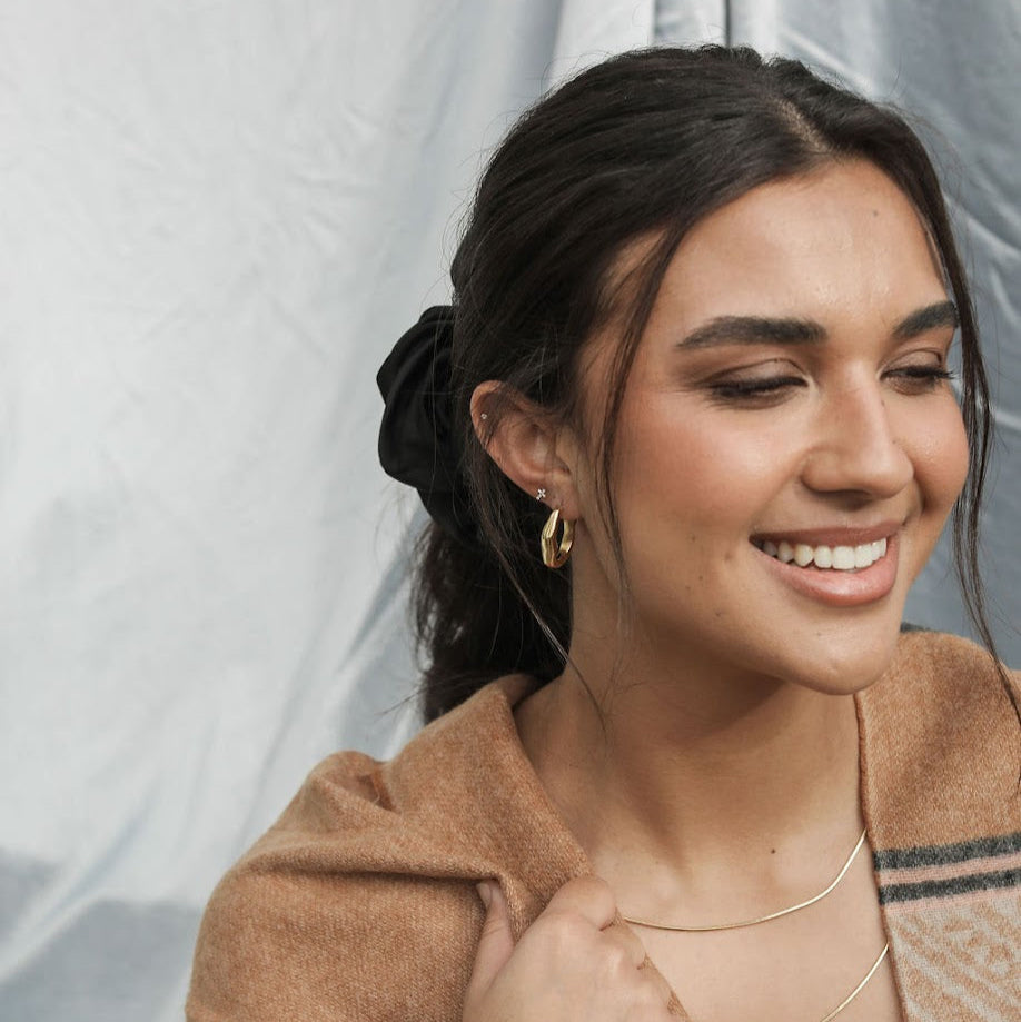 Woman wearing a brown scarf with gold hoop earrings with a blurred background