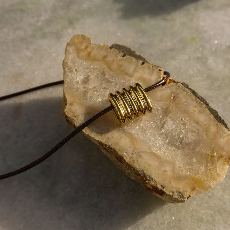 Cord necklace with a gold pendant on a stone surface