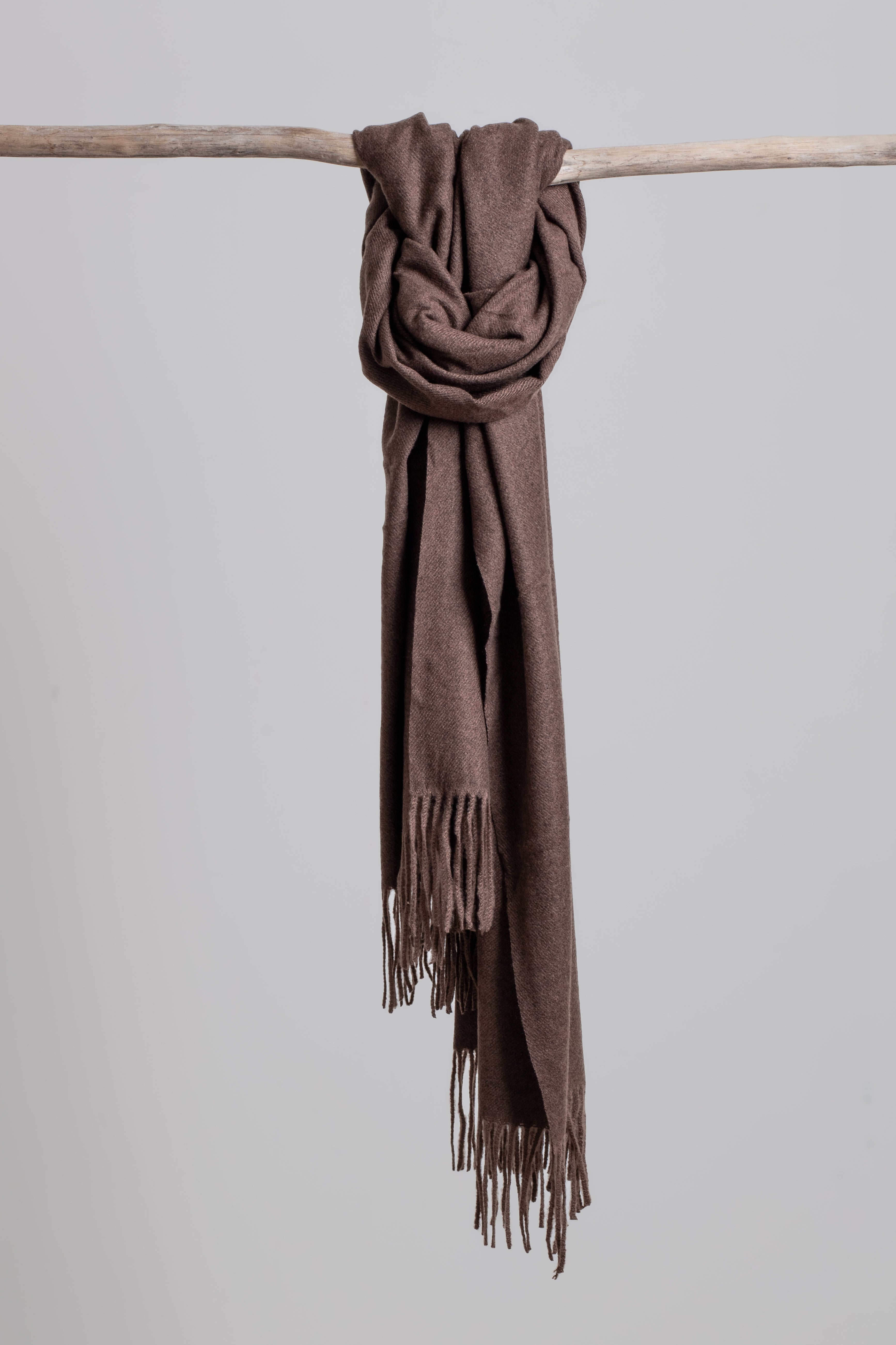 chocolate brown scarf with fringes draped over a wooden stick on a light gray background