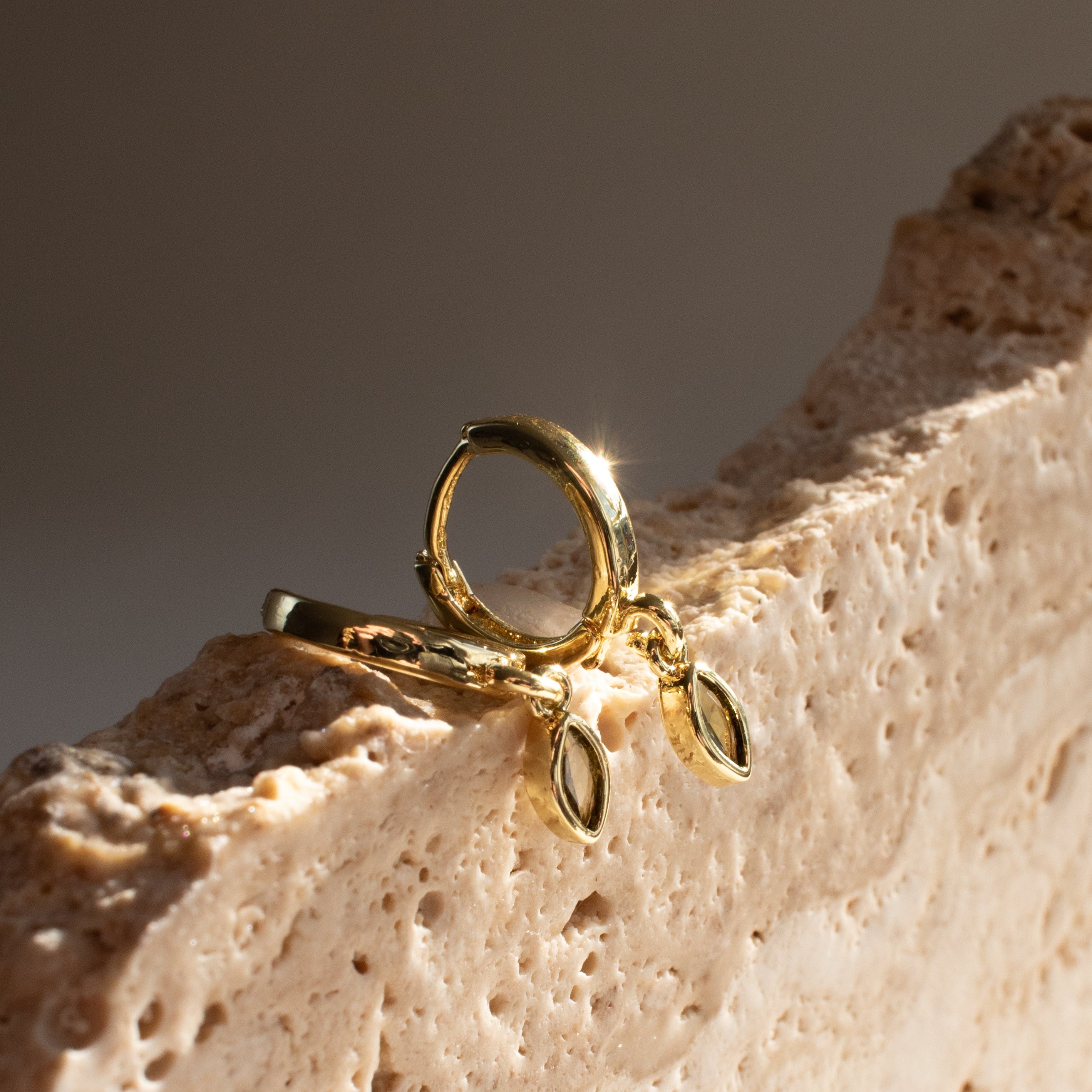 Gold earrings with peridot marquise shaped designs on a textured stone surface