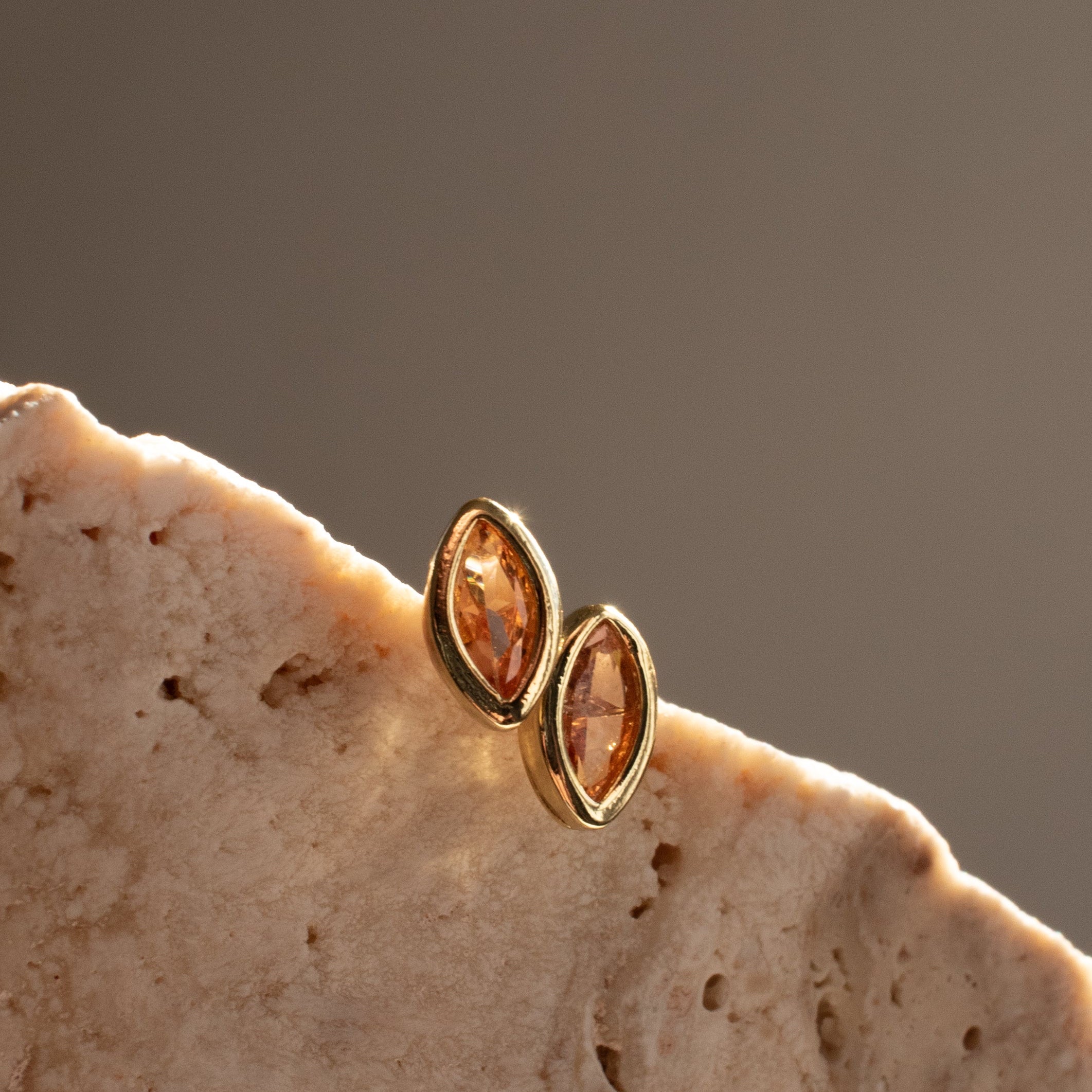 Gold earrings with citrine gemstones on a beige stone surface