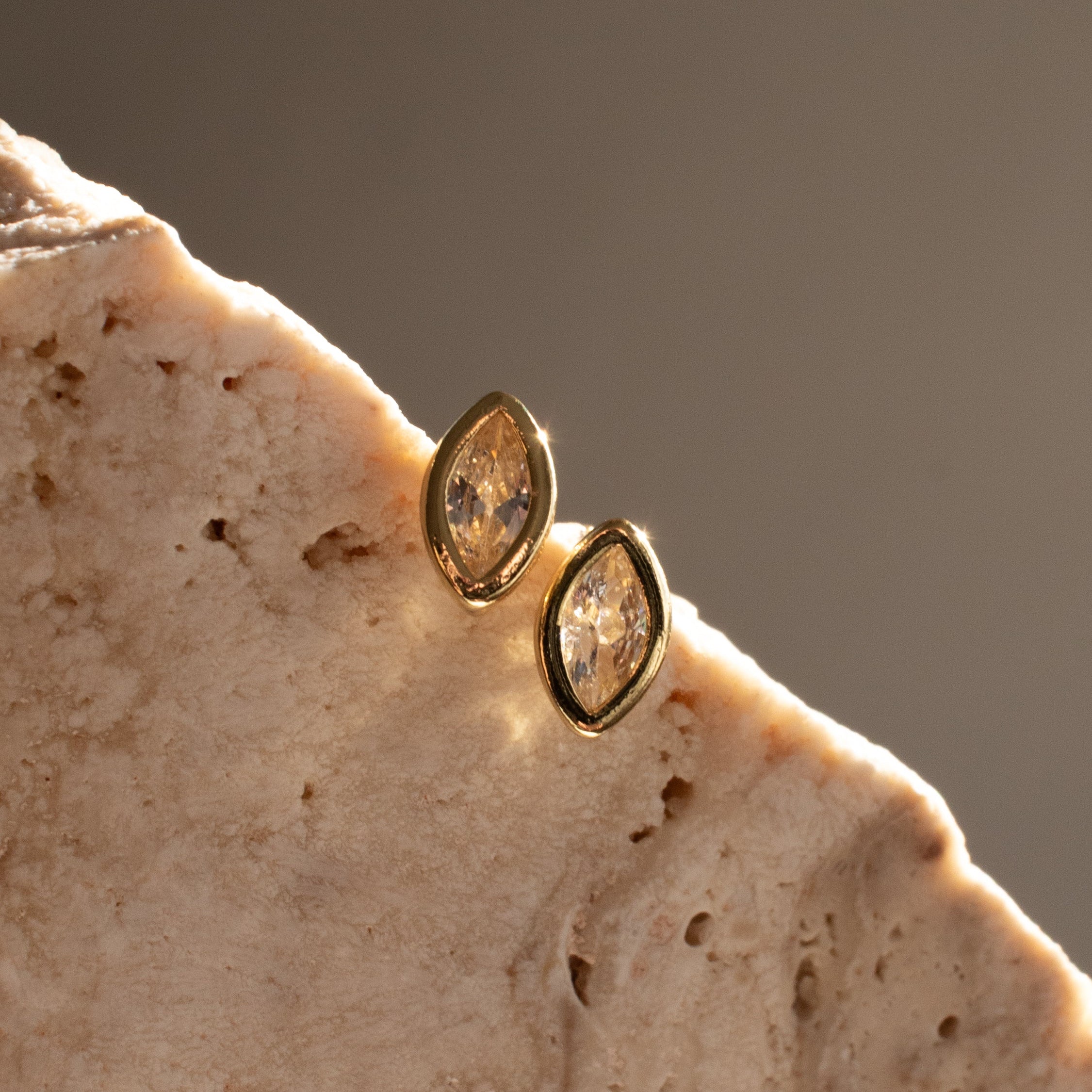 Gold earrings with marquise-shaped diamond stones on a textured stone surface