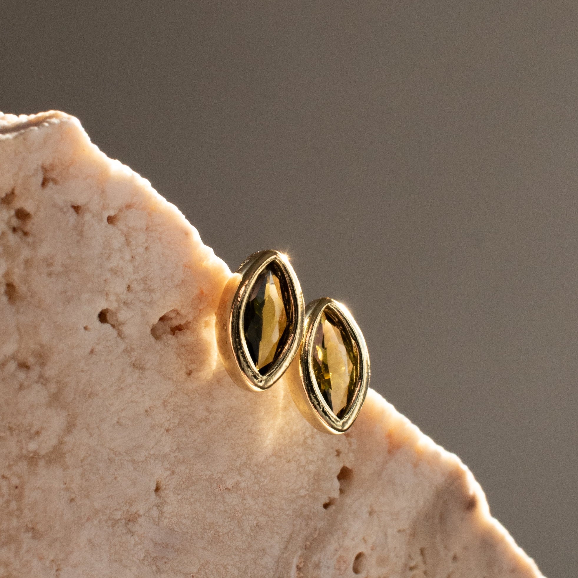 Gold earrings with peridot stones on a textured stone surface