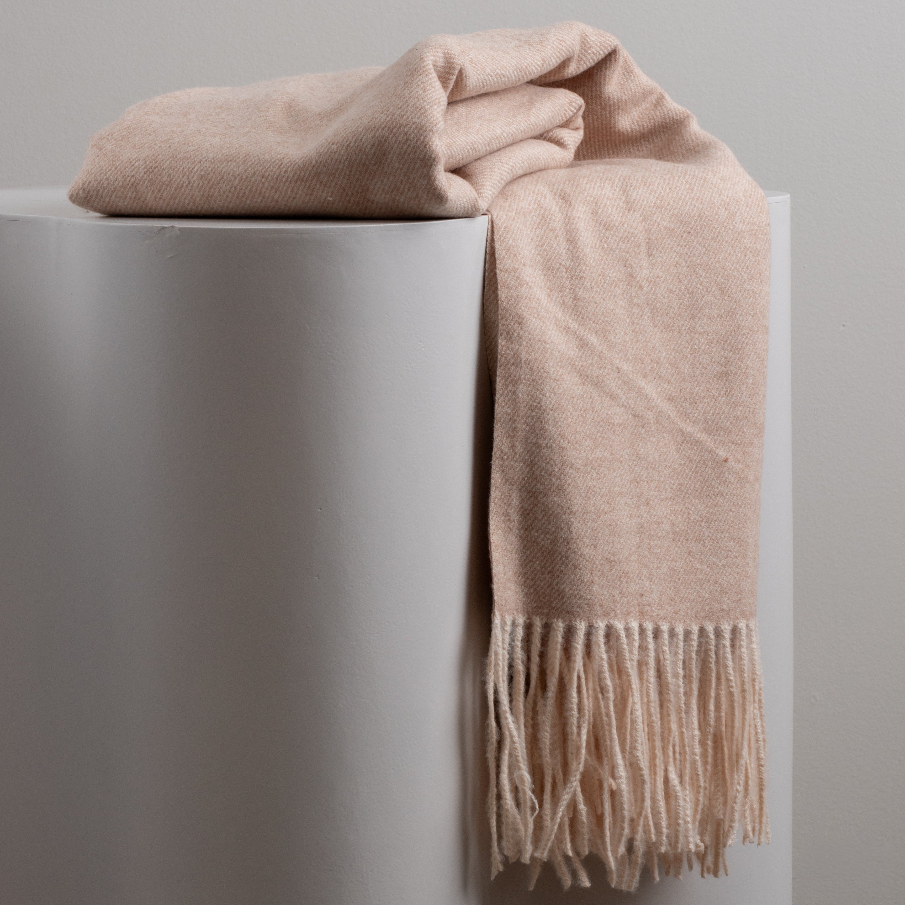 Creamy beige scarf with fringe draped over a white surface against a light gray background