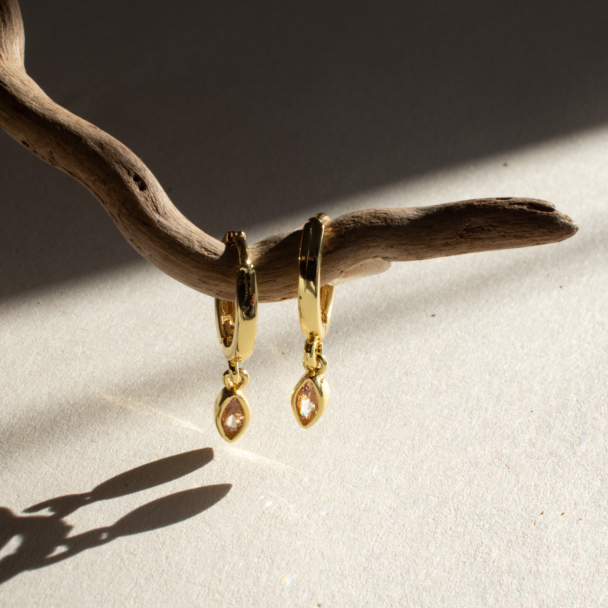 Gold citrine marquise shaped earrings hanging from a branch on a textured surface