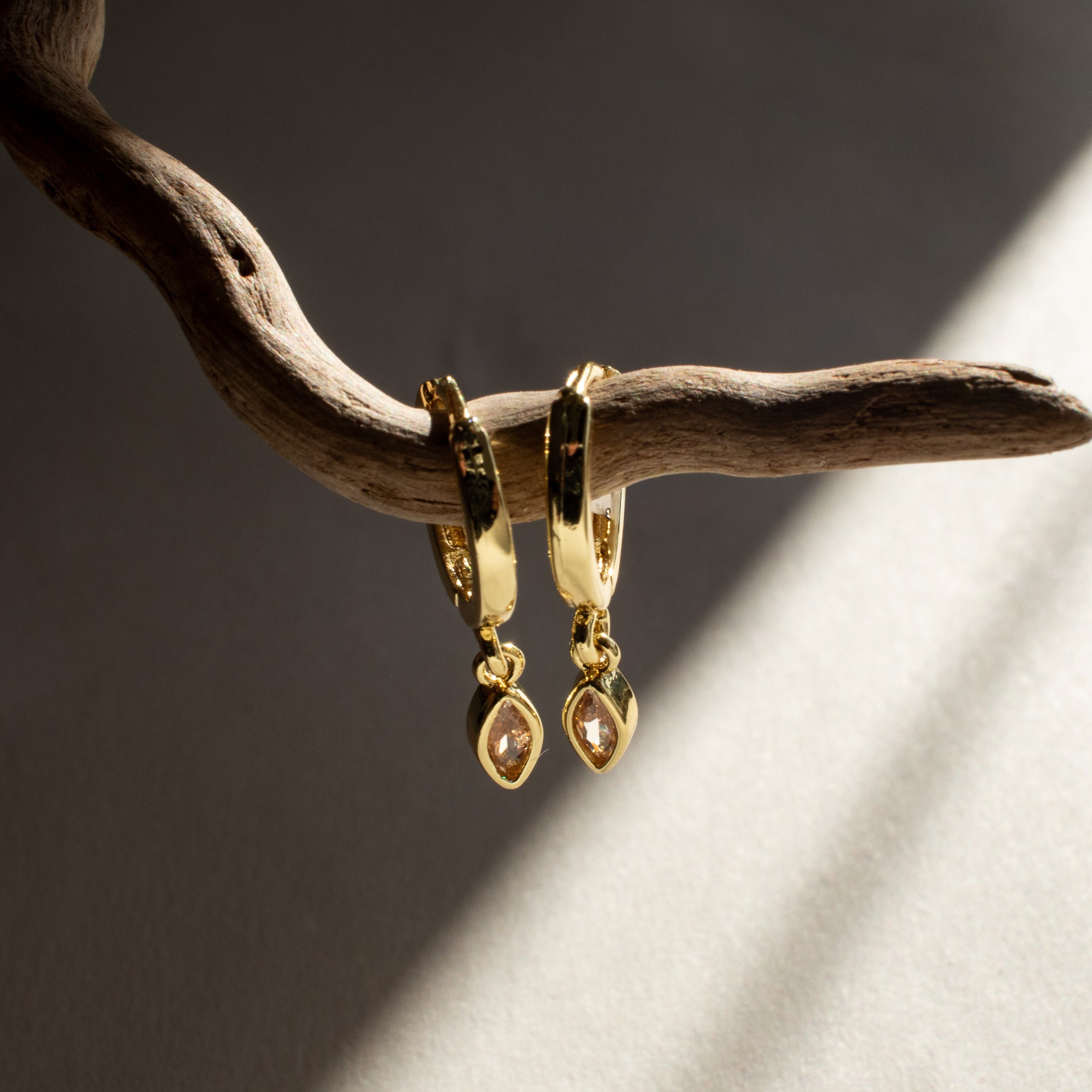 Gold and citrine earrings hanging from a branch with a soft light background