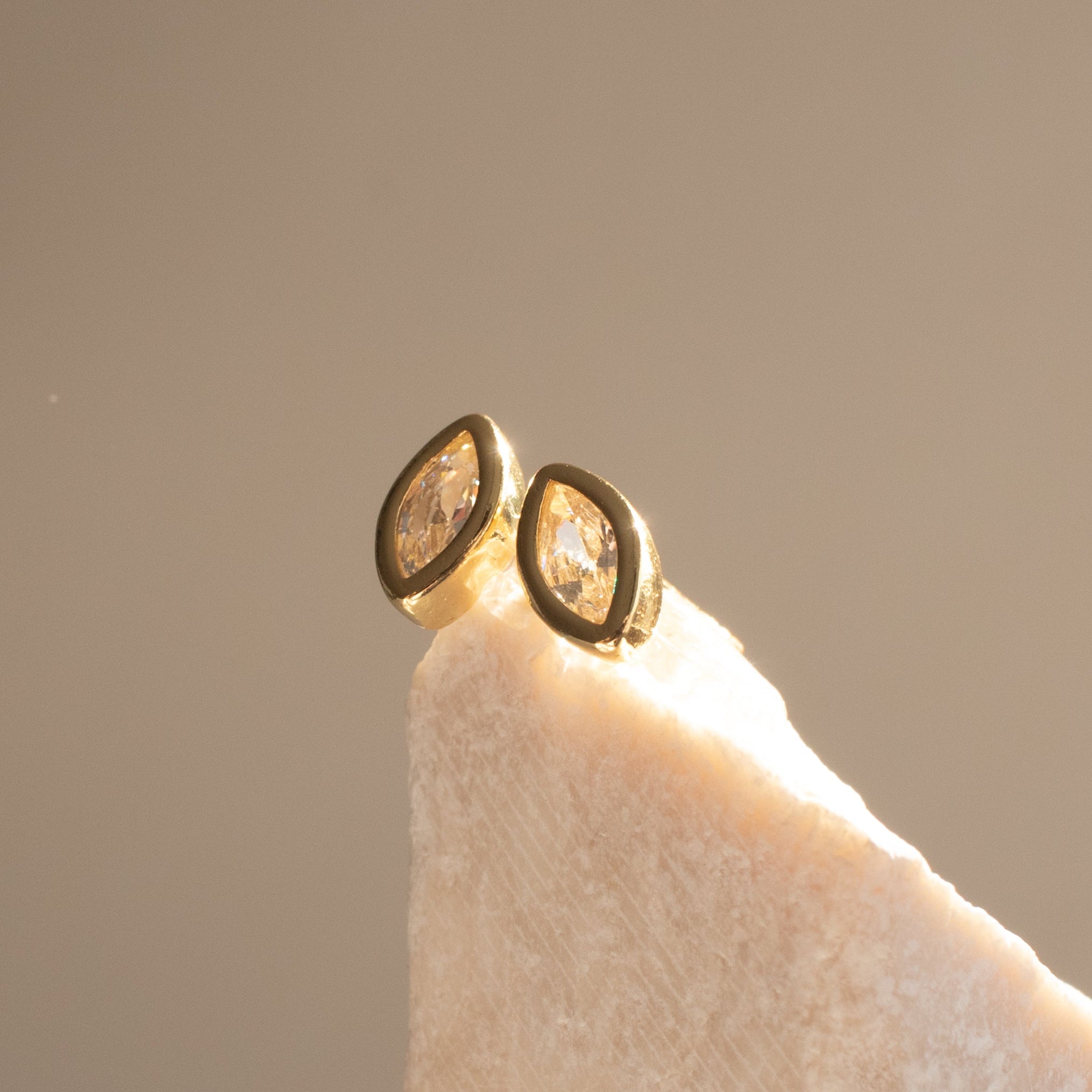 Gold earrings with marquise diamond stones on a light stone surface