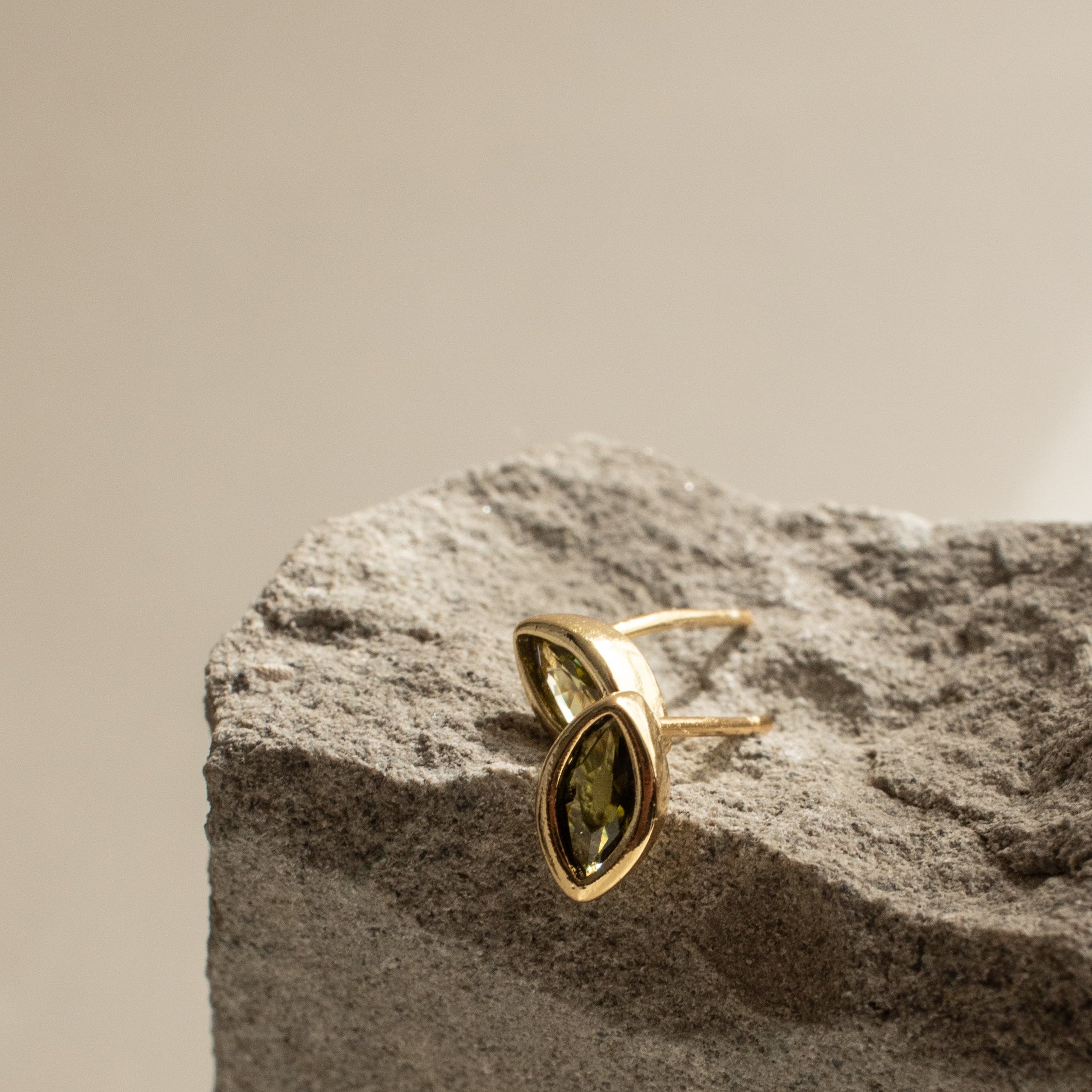 Gold Earrings with a peridot green gemstone on a textured stone surface