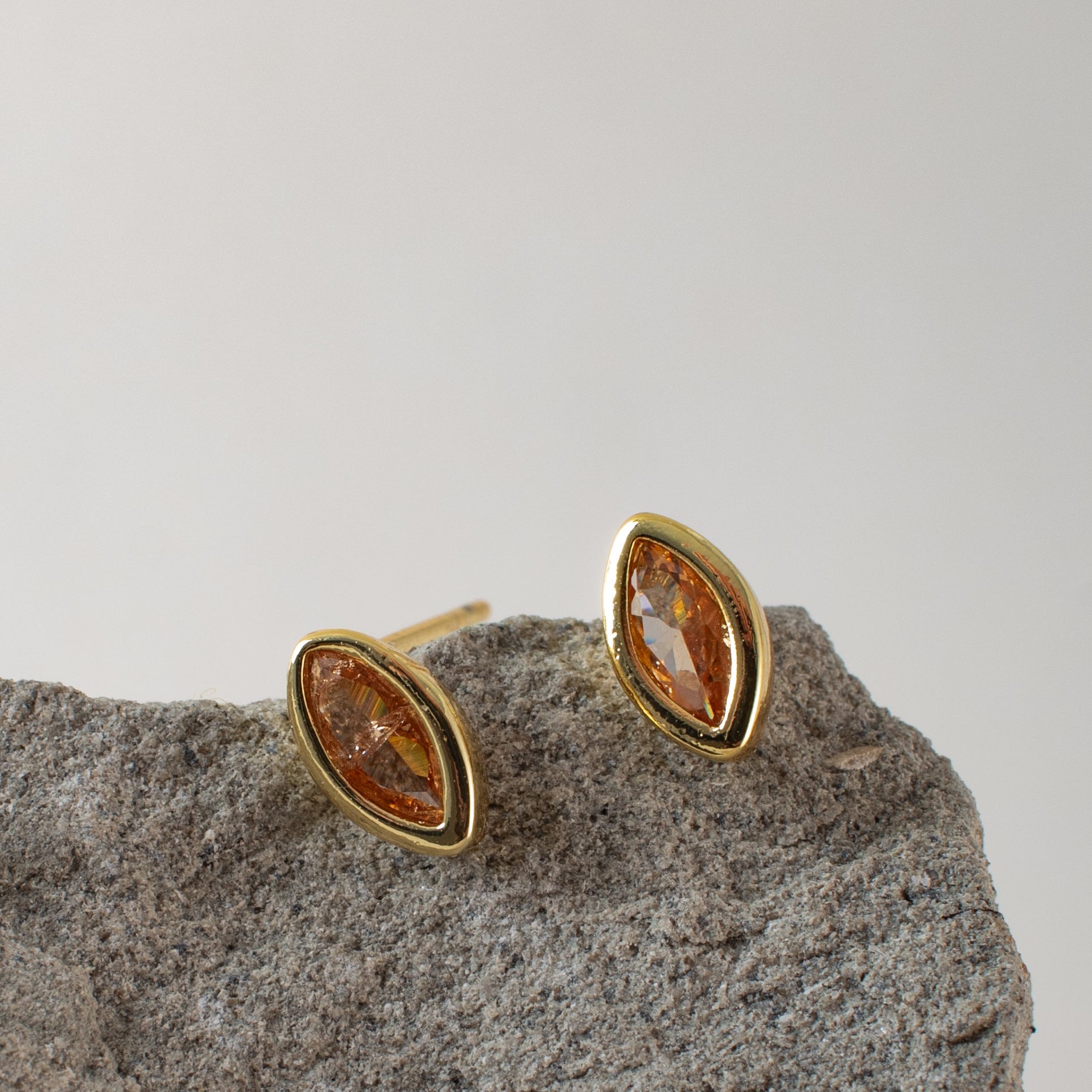 Pair of gold earrings with citrine gemstones on a gray stone surface.