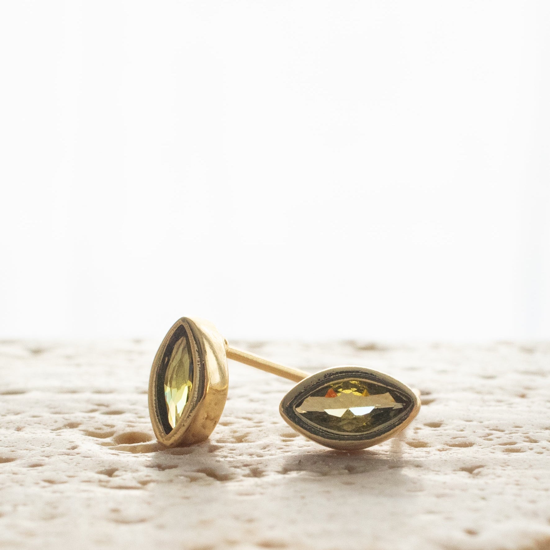 Gold earrings with peridot gemstones on a textured surface