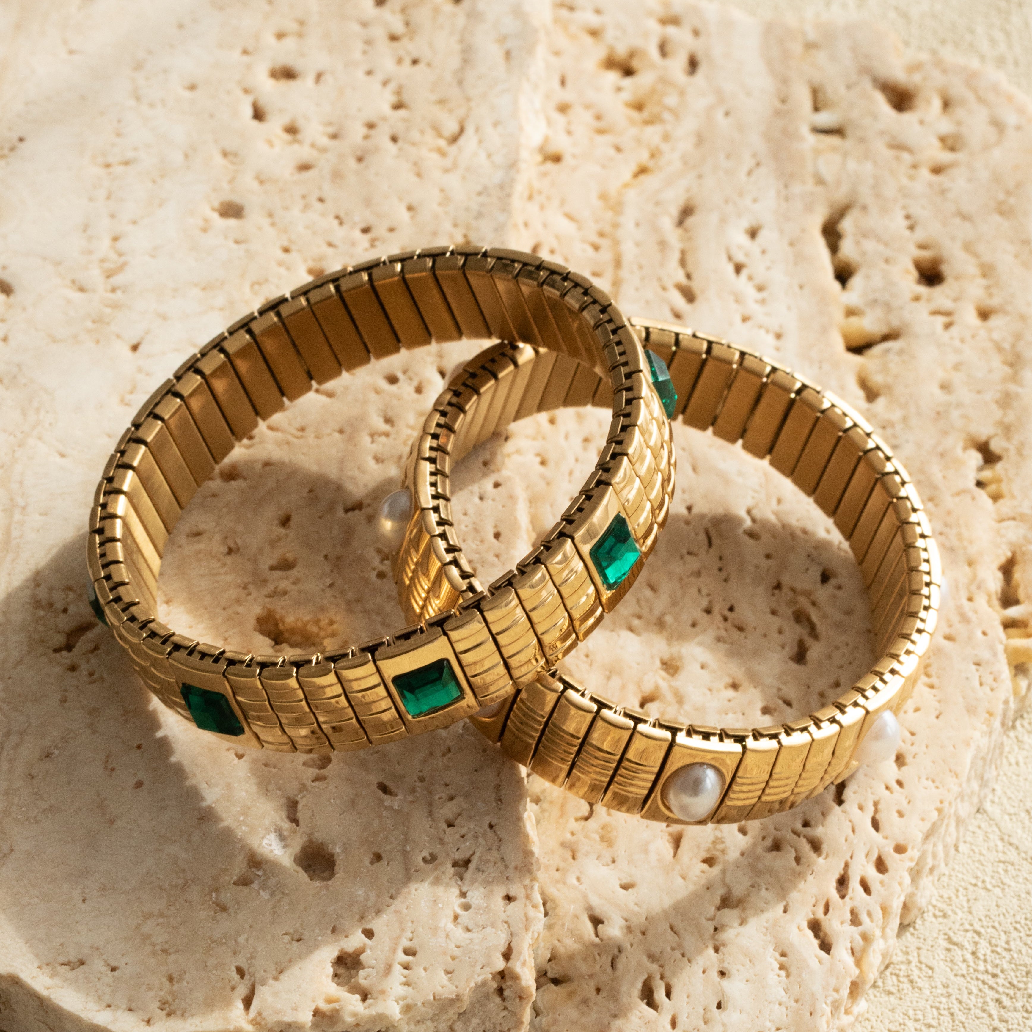 Gold emerald and pearl strap bracelets on a textured stone surface