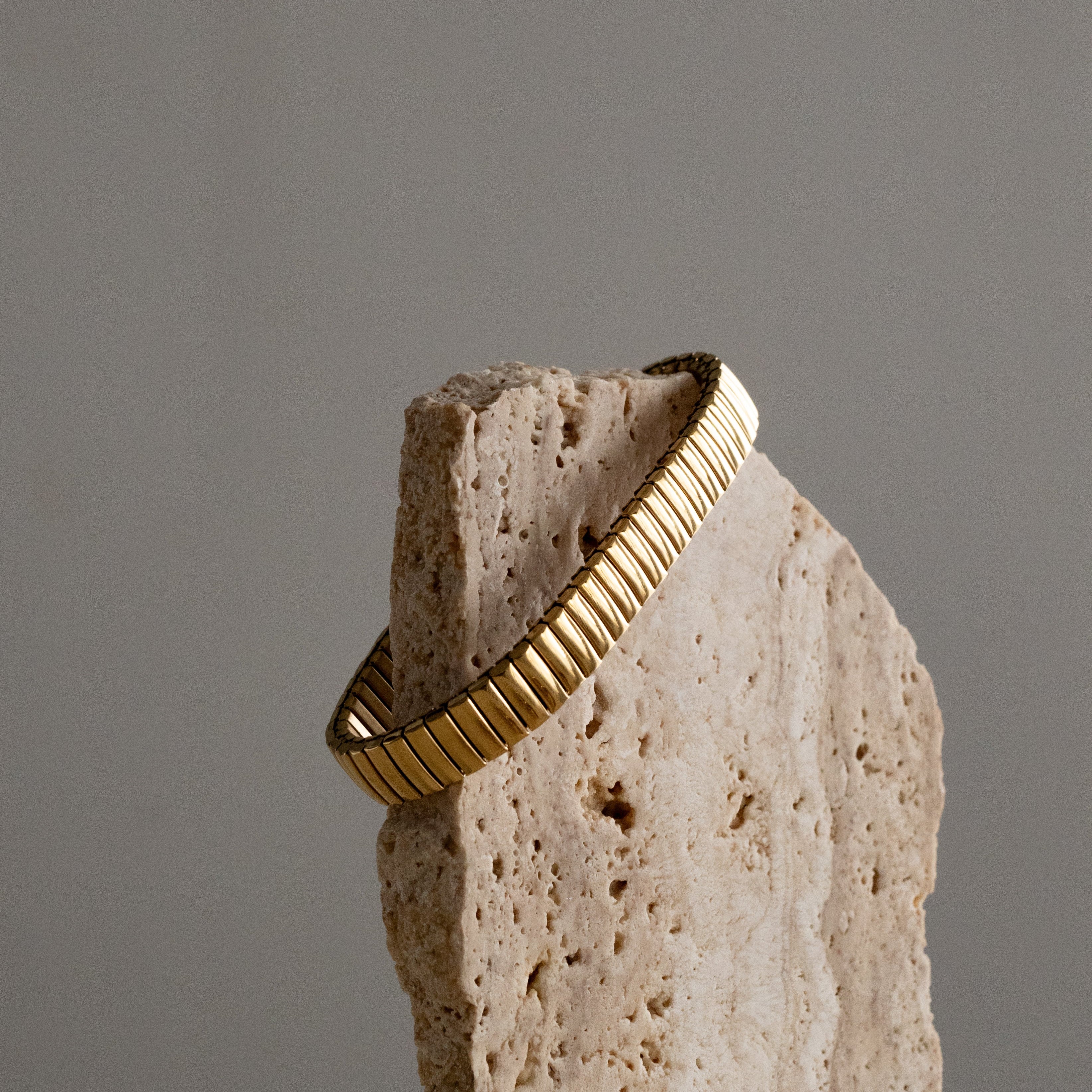 Gold flexible strap bracelet on a textured stone