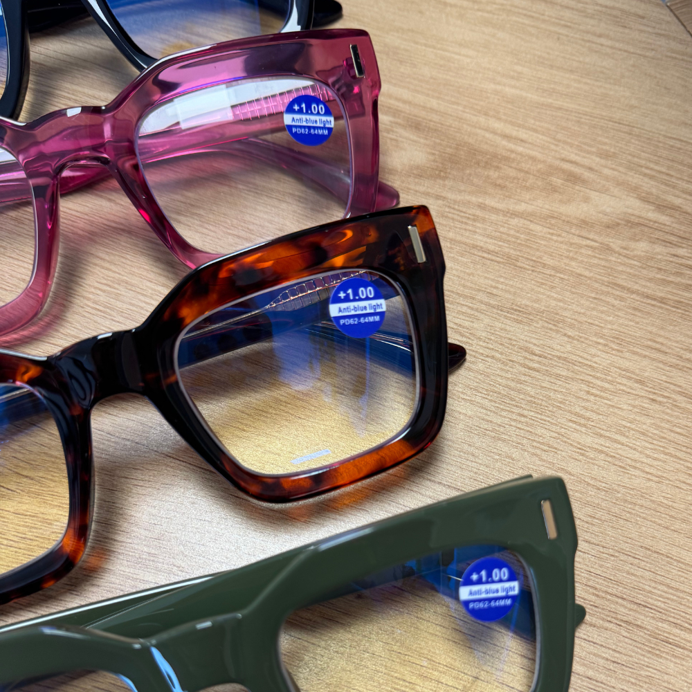 Three pairs of eyeglasses with blue labels on a wooden surface