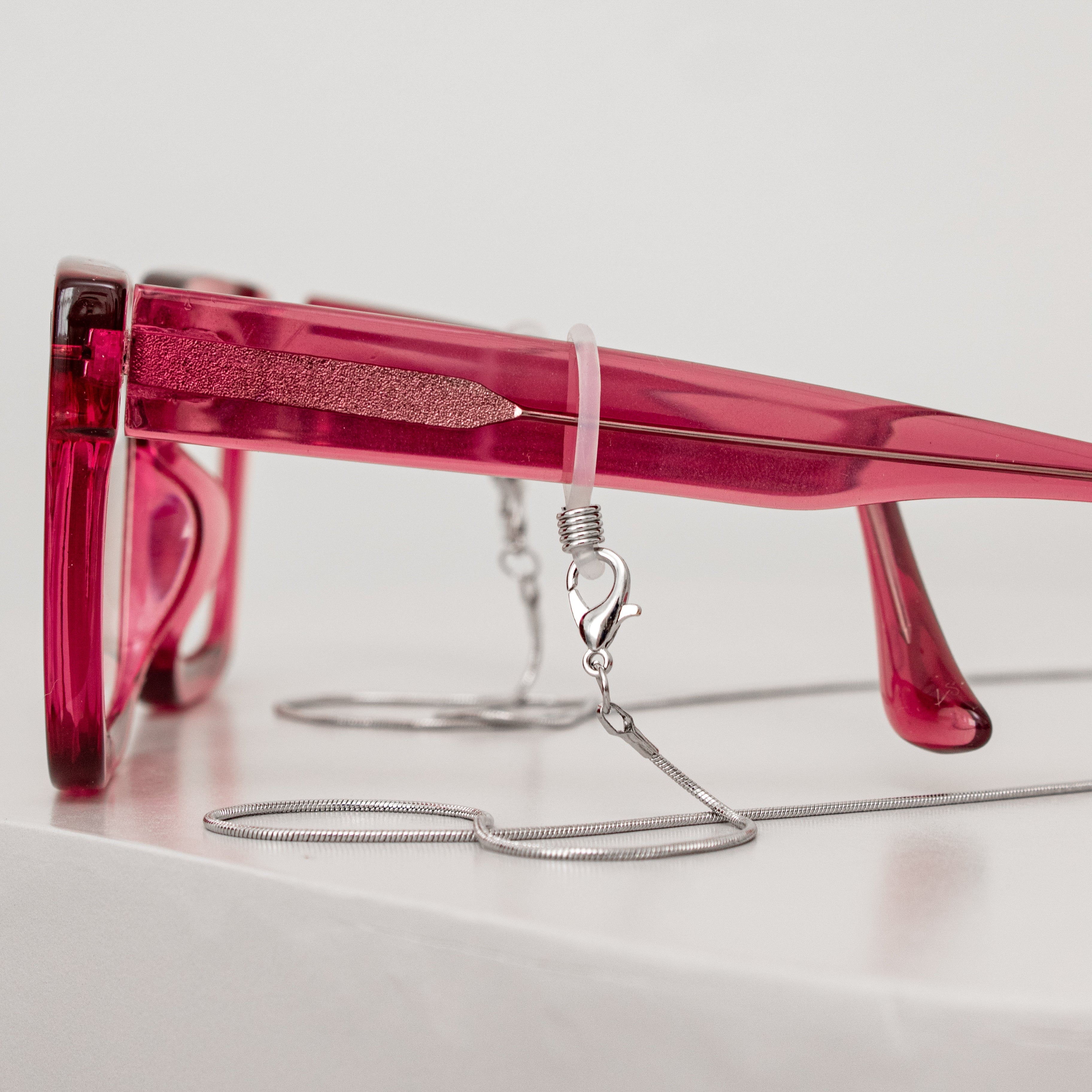 Pink sunglasses with a chain on a white surface