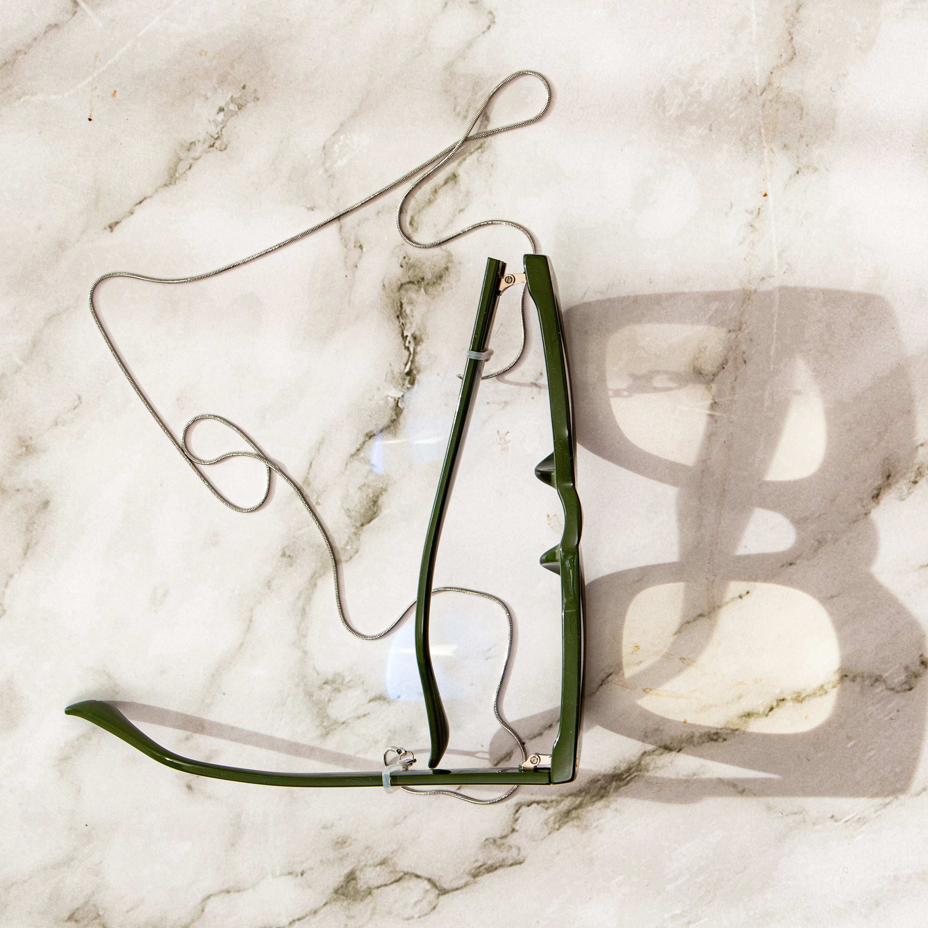 Olive green glasses with chain on a marble surface