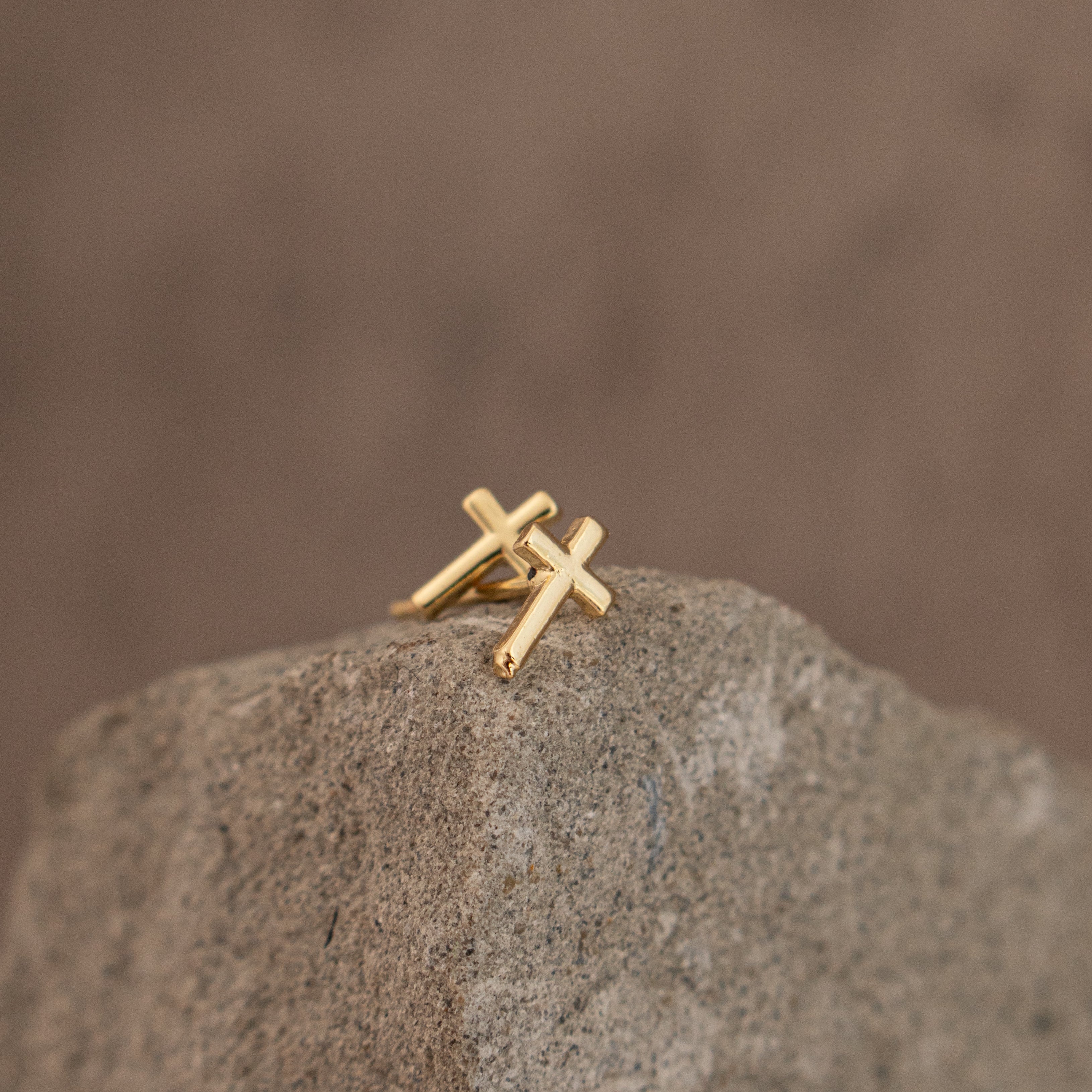 Gold cross-shaped earring on a stone surface with a stone background