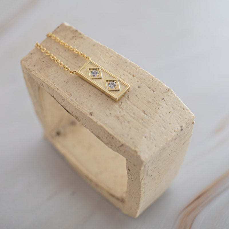 Gold Queen of the Foxes necklace with a double diamond pendant on a ceramic stand against a white background