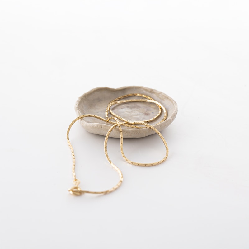 Gold necklace on a white surface with a small stone dish.