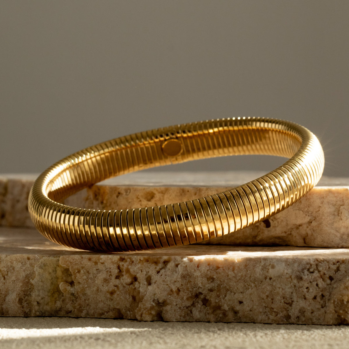 Queen of the Foxes gold banded bracelet on a piece of pale stone against a neutral background.