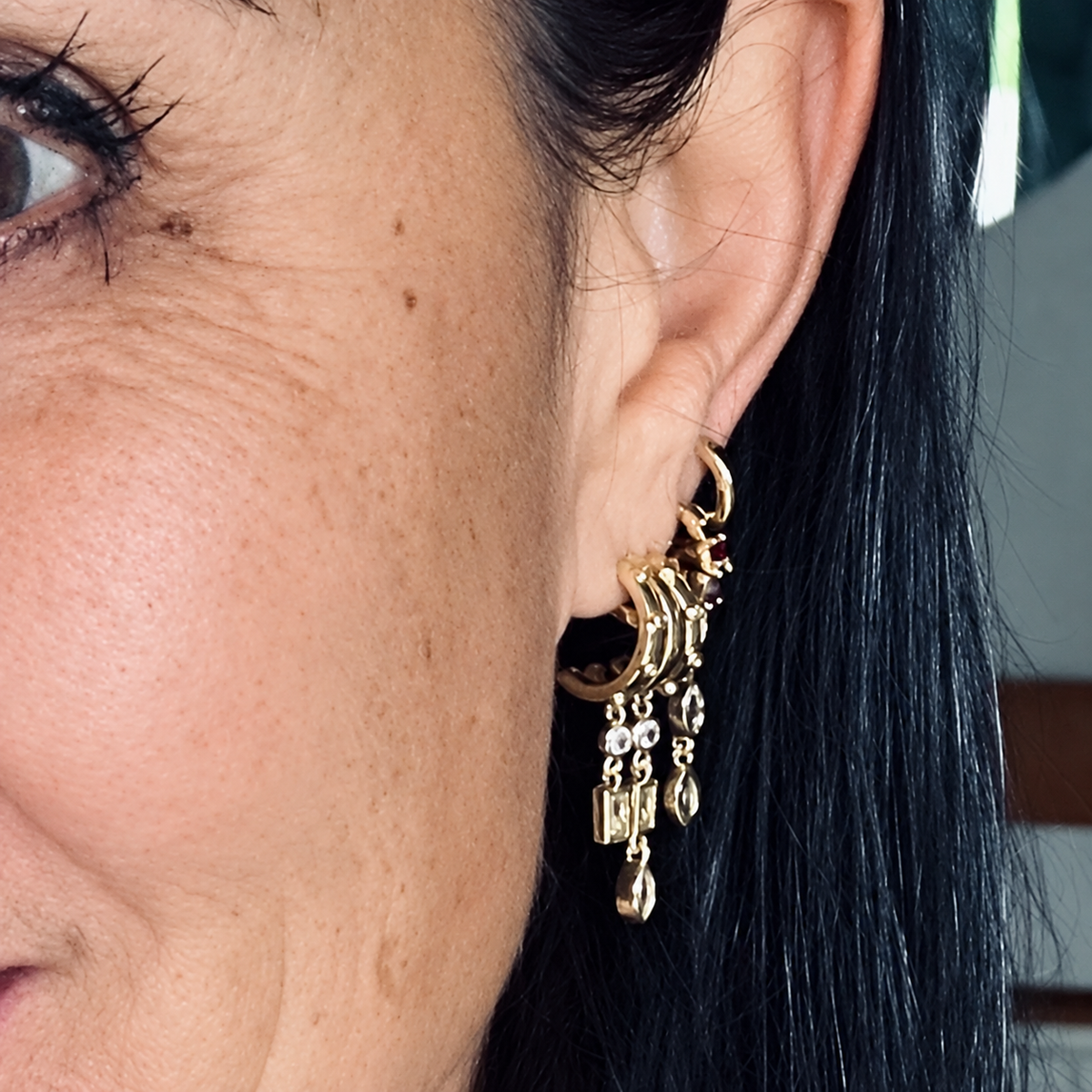 Close-up of Marquise Triple Drop earrings worn in a layered gold earring stack with hoops and other dangling charms.