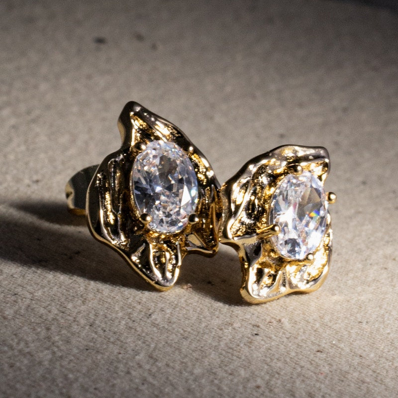 Close-up of clear oval cubic zirconias held in sculptural gold settings with rustic folds and irregular edges.