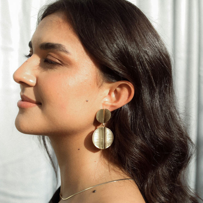 Woman wearing gold earrings with a neutral background