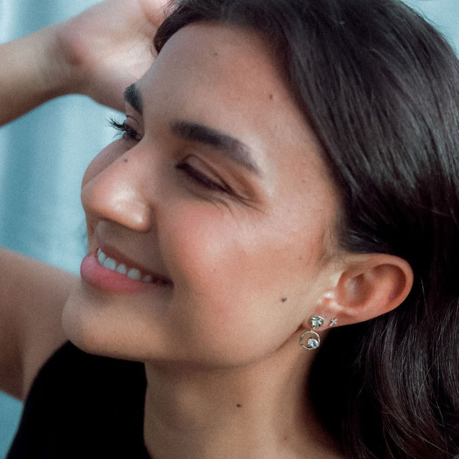 Woman with dark hair and earrings, wearing a black top against a blurred background