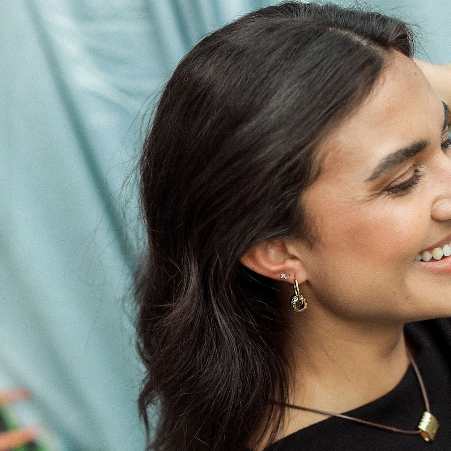 Woman with dark hair and earrings smiling against a light blue curtain background