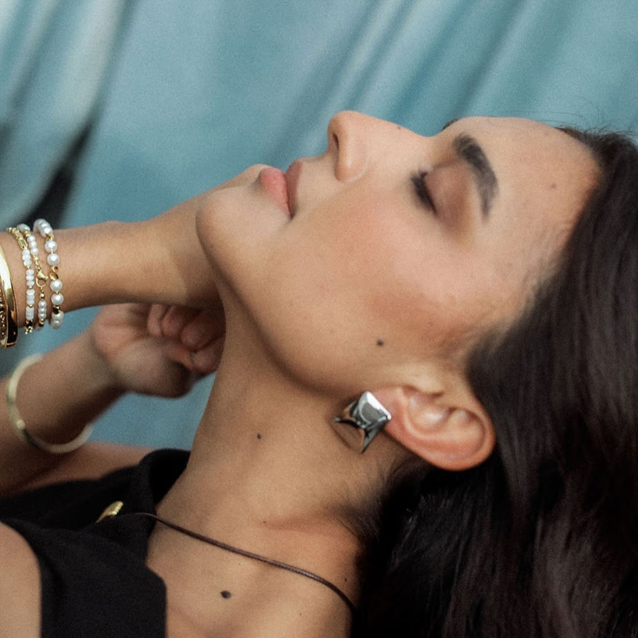 Woman with silver earrings and bracelet stack with  a blue background