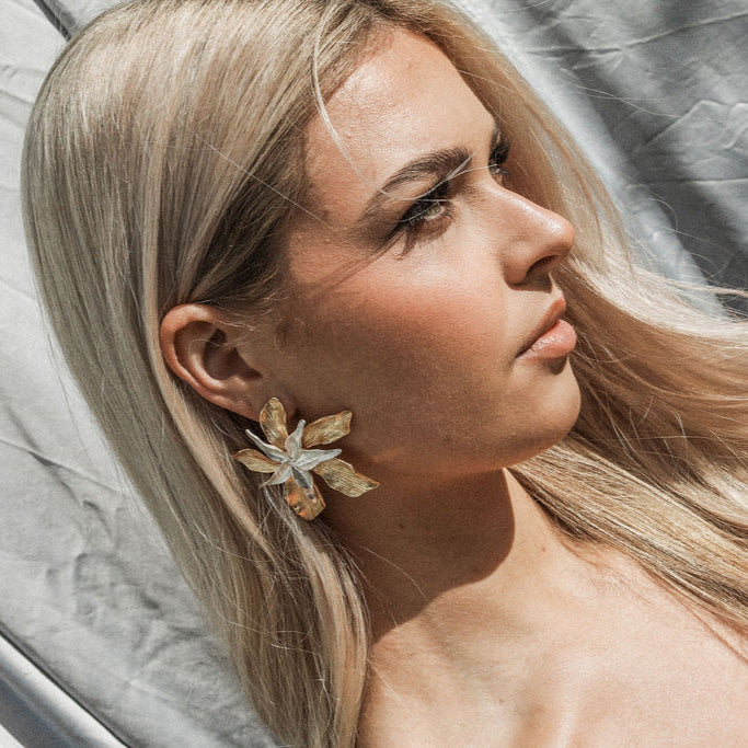 Woman with long blonde hair wearing a floral earring, in front on a textured surface.