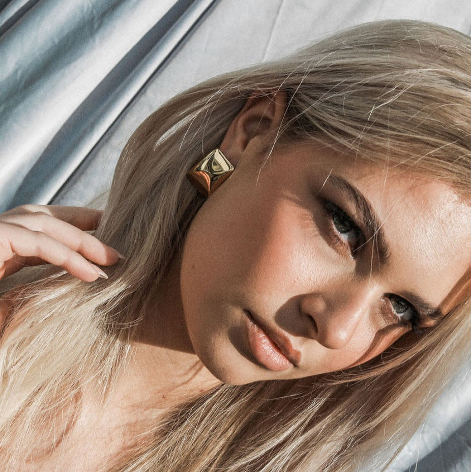 Woman with blonde hair and gold earrings against a neutral background