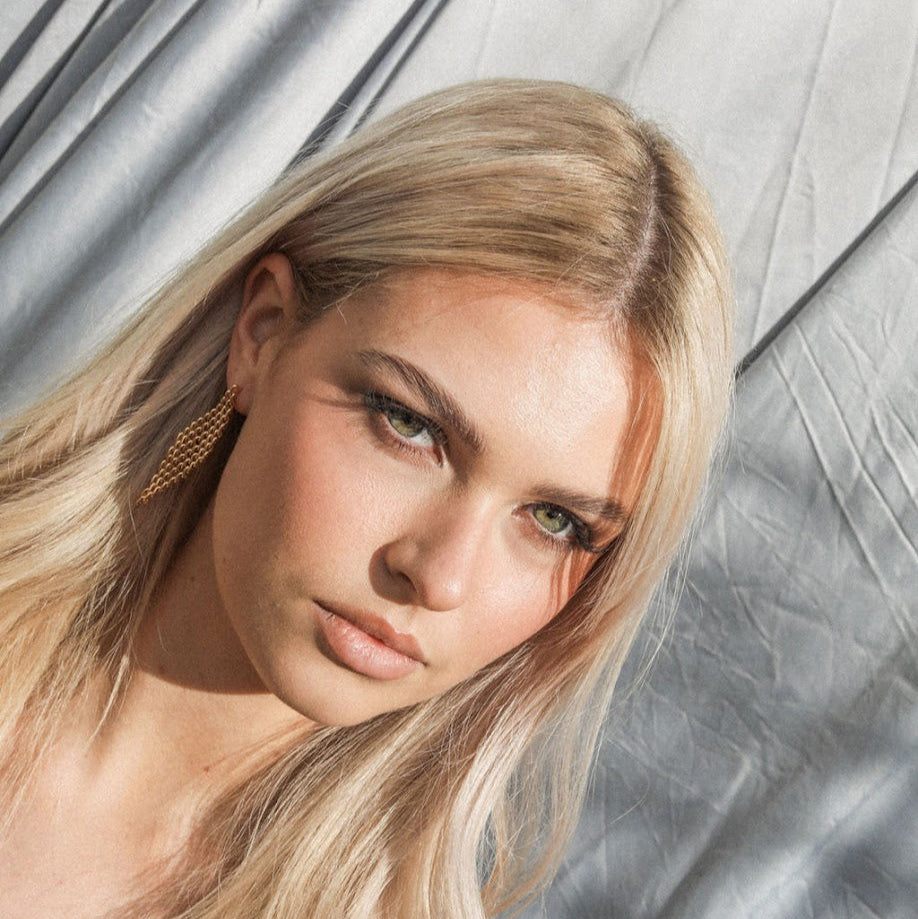 Woman with blonde hair and mesh diamond earrings against a textured gray background