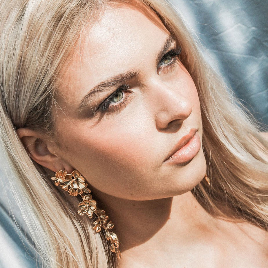 Woman with blonde hair and gold statement floral earrings against a neutral background