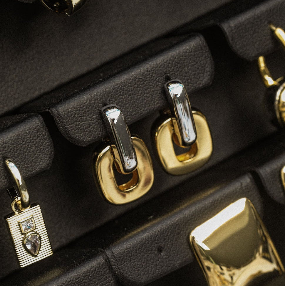 Close-up of gold and silver earrings on a black jewelry display.