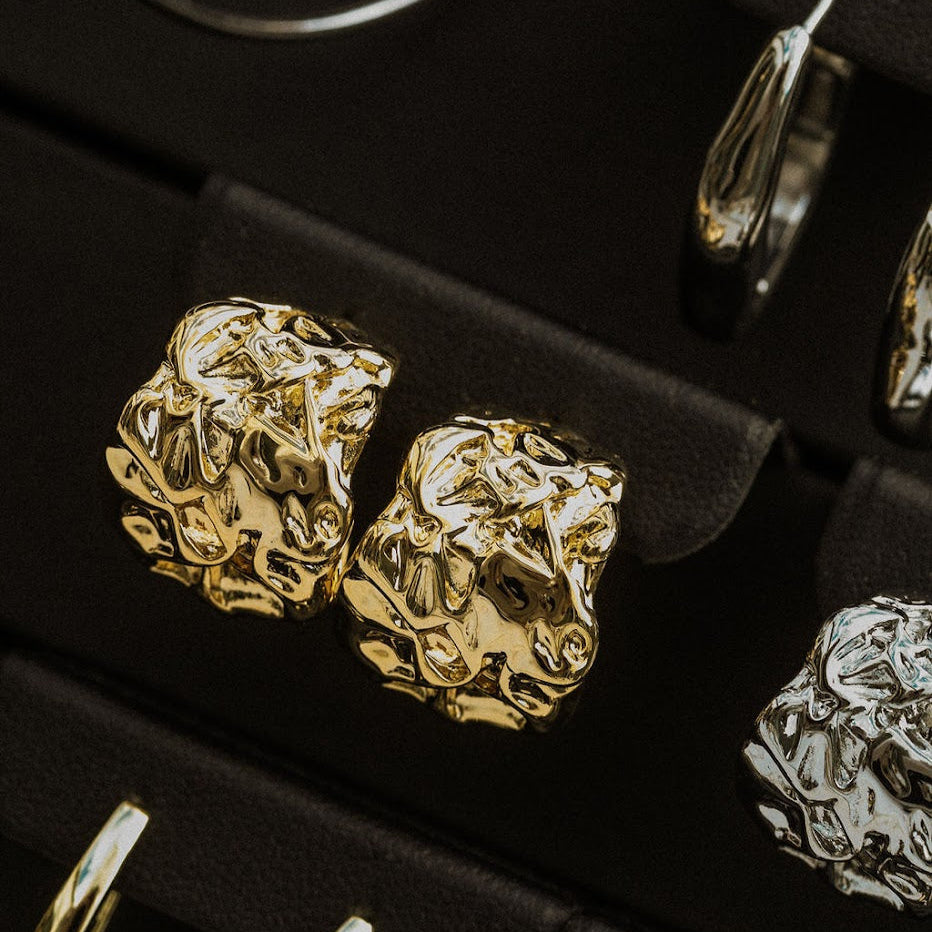Gold and silver ruched earrings on a black jewelry display.