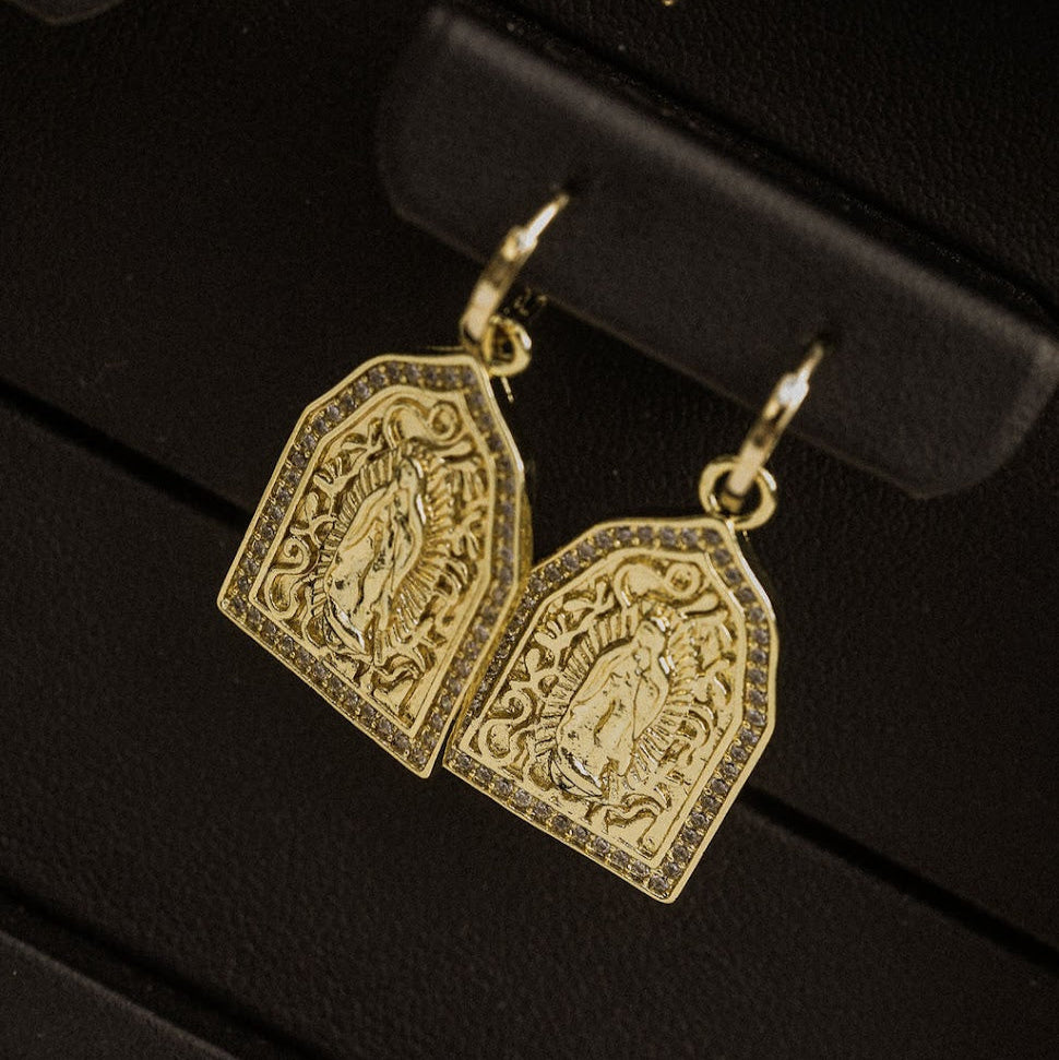 Gold earrings with engraved designs on a black stand.