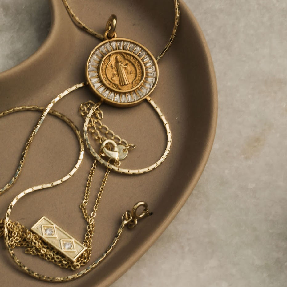 Gold necklaces with intricate designs on a brown ceramic dish.