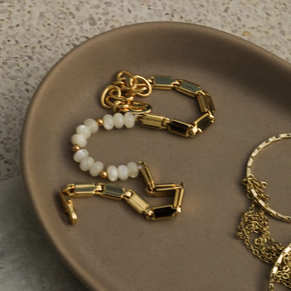 Gold and beaded bracelets on a beige plate with a neutral background