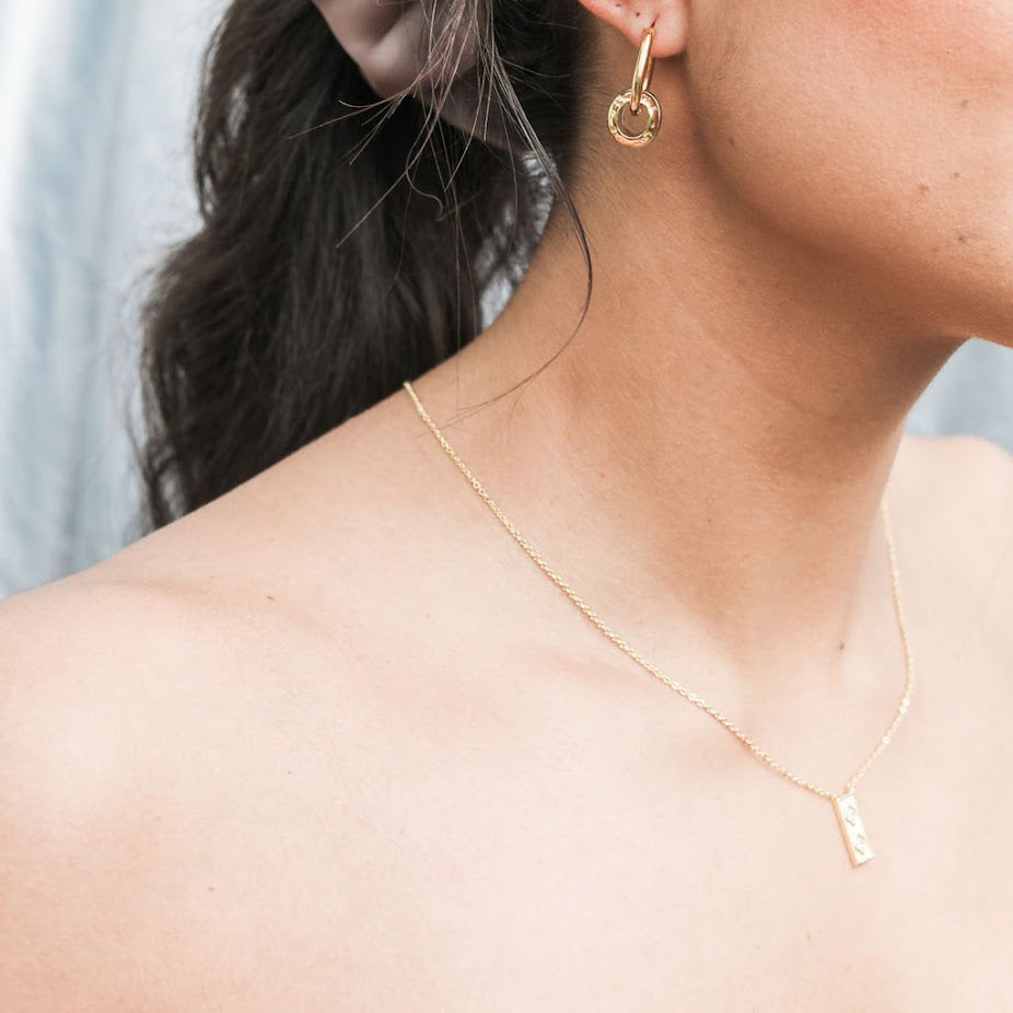 Close-up of a woman wearing gold hoop earrings and a necklace with a blurred background