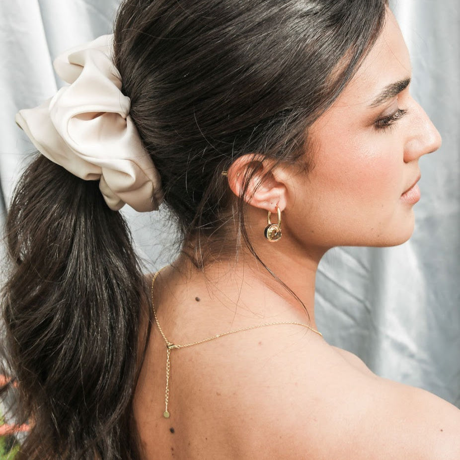 Woman with a fine necklace, earrings, ponytail and hair scrunchie against a neutral background