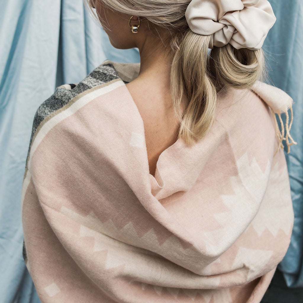 Woman with styled hair and a pink scrunchie against a light blue curtain background
